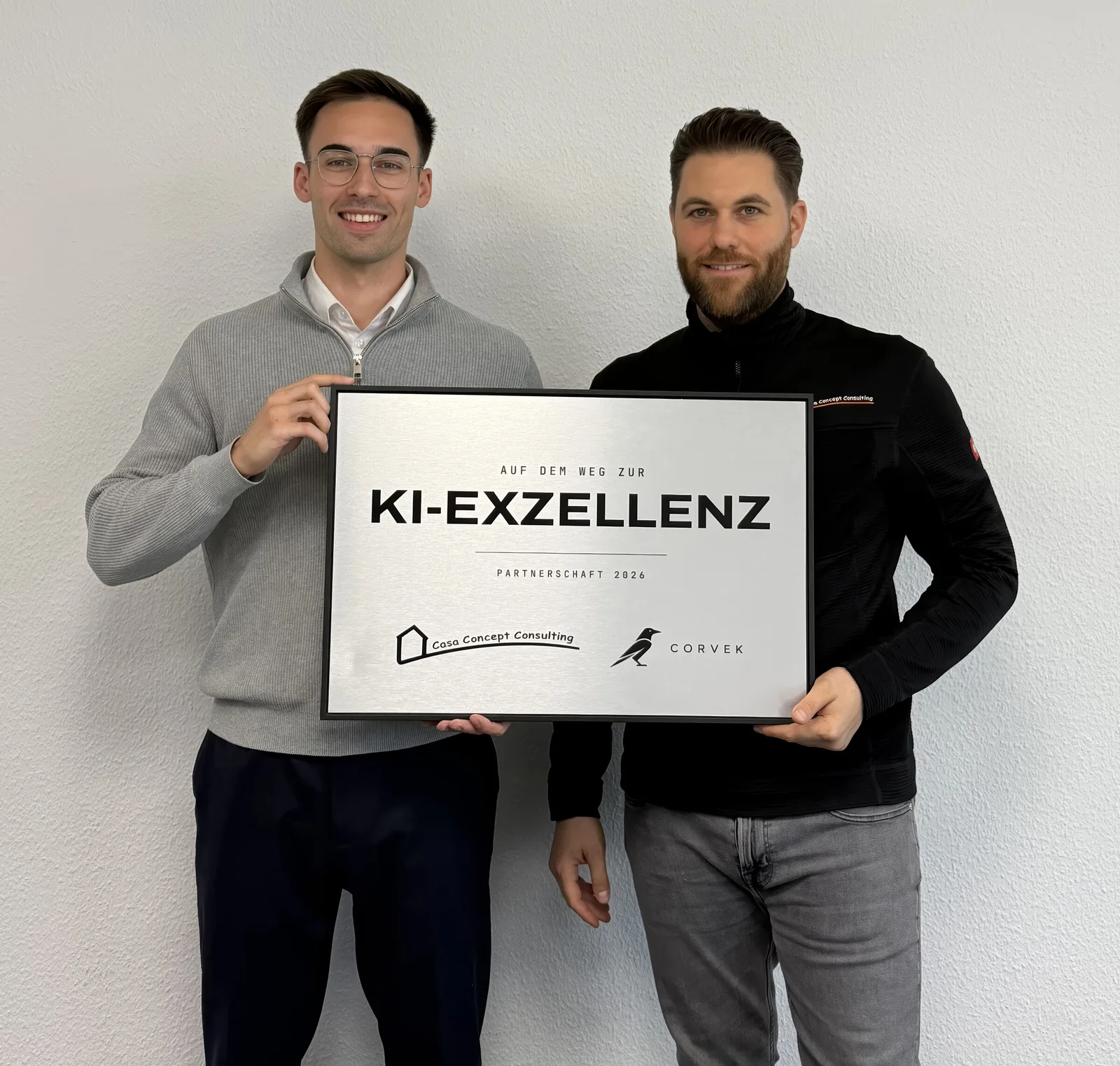 Lennart Dürr und Giovanni Hierl halten das Schild „Auf dem Weg zur KI-Exzellenz, Partnerschaft 2026“